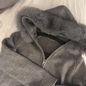 Grå stickad jacka med pälshuva - Mysig grå alessa jacka, Enkel och stilren design. Säljs då den aldrig har kommit till användning. Den är i storlek S men passar även xs. OBS:(inte mina bilder utan tog dom från alessa hemsidan, hör av er för privata bilder med den på. 