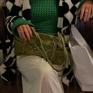 Grön croco axelväska med silverdetaljer - Säljer en grön axelväska i croco-mönstrat syntetmaterial med snygga silverringar och spänndetaljer. Väskan har flera fack, dragkedja i mitten och långa handtag som gör den enkel att bära på axeln. Perfekt för dig som vill sticka ut med en cool accessoar. Använt denna en gång! Så gott som ny. Älskar denna men har för många väskor som inte kommer till användning 🥹villig att gå ner i pris vid snabb affär! 💚💚