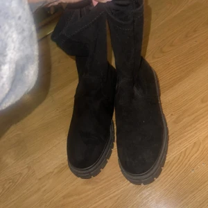 Svarta mockaboots med grov sula - Säljer ett par svarta boots i mocka med chunky, mönstrad sula. Skorna har rund tå och är helt svarta, perfekta för höst och vinter. De är höga och har en stilren look som passar till många outfits.