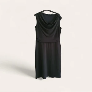 Svart ärmlös klänning från Esprit - Svart ärmlös klänning från Esprit med draperad halsringning och markerad midja. Klänningen har en klassisk, rak passform och är tillverkad i ett mjukt, följsamt material som ger en snygg siluett. Perfekt för dig som gillar stilren och tidlös design. Byst: ca 47 (upp till 54) × 2 cm. Midja: ca 40 (upp till 45) × 2 cm