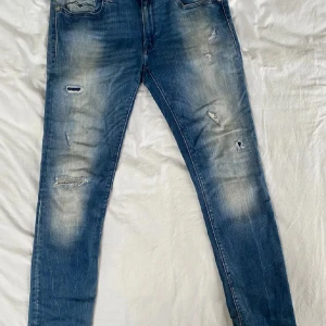 Blå slitna jeans med skinny fit - Säljer ett par blå jeans med slitningar och snyggt tvättad look. Jeansen har smal passform och klassiska fem fickor. Materialet är denim och de har en modern, lite ruff stil som passar perfekt till sneakers och hoodie.