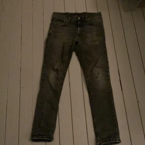 Grå skinny jeans från Nudie Jeans - Säljer ett par grå skinny jeans från Nudie Jeans i storlek 28/30. Jeansen har klassisk femficksdesign, smal passform och är tillverkade i stretchig denim för en bekväm känsla. Snyggt slitna detaljer och diskret tvättad look.
