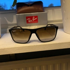 Ray-Ban boyfriend - Snygga svarta Ray-Ban solglasögon med rektangulär form och tonade bruna linser. Bågarna är i plast med metallinslag och har diskret Ray-Ban-logga på sidan. Perfekt för dig som vill ha en klassisk och stilren look.