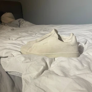 Beige sneakers från Axel Arigato - Snygga beige sneakers från Axel Arigato i mocka med minimalistisk design och platt sula. Skorna har diskret logga på sidan och under sulan, samt en rund tå. Perfekta för dig som gillar cleana och stilrena sneakers. Skolåda fås med