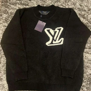 Svart stickad tröja Louis Vuitton - Svart stickad tröja från Louis Vuitton med stor vit LV-logga på bröstet. Tröjan har rund halsringning, ribbade muddar och är långärmad. Perfekt för dig som vill ha en lyxig och stilren look med streetkänsla.