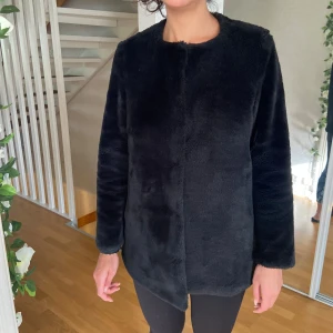 Svart pälsjacka i fuskpäls st.S - Mysig svart pälsjacka i fuskpäls med rund halsringning och raka, långa ärmar. Jackan har en stilren och enkel design utan synliga knappar eller dragkedja, perfekt för dig som vill ha en clean look. Passformen är normal och jackan är något längre i modellen.knappt använd. Mycket bra skick.Stradivarius svart jacka, storlek S