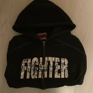 Svart hoodie från Fighter Gear - Mörk blå hoodie från Fighter Gear med stort vitt tryck 'FIGHTER' över bröstet. Skick 8/10. Riktigt fräsch och vintage. Storlek S. Skriv vid minsta fundering!