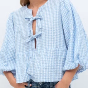 Blåvit rutig blus med rosetter - Supersöt blus i blåvitt rutigt mönster med volang nertill och puffiga trekvartsärmar. Blusen har två rosetter framtill. Perfekt till jeans för en, passar i alla årstider💙🤍