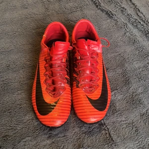 Nike Mercurial  - Säljer ett par NIKE MERCURIAL VAPOR XI AG FIRE. Sällsynta skor som inte längre säljs. Vapor 11 som är mångas favorit modell genom tiderna. Skicket på skorna är slitet. Dobbarna är väldigt slitna och korta. Sulan har släppt lite lätt på sina ställen. Skicket skulle jag säga är 3/10. Slitna, går att använda okej men på högre nivå skulle jag hålla dom på träningsplanen eller hyllan. 