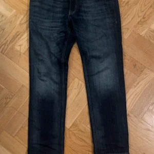 Mörkblå jeans Jack & Jones Regular Clark - Snygga mörkblå jeans från Jack & Jones, modell Regular Clark. Klassisk femficksdesign med raka ben och kontrastsömmar. Jeansen har en straight passform och är tillverkade i slitstarkt denimtyg. Perfekta för en avslappnad och stilren look.