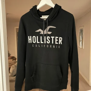 Svart hoodie från Hollister - Trendig och snygg hollister hoodie i storlek S. Tröjan är 8/10 i skick skulle jag säga med endast en liten defekt på vänster armen. Om frågor eller funderingar så skriv! 