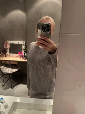 Grå stickad tröja med rund hals - Mysig grå stickad tröja med rund halsringning och ribbade muddar. Tröjan har en relaxed fit och är perfekt för kyliga dagar. Enkel och stilren design som passar till det mesta. Snygg att matcha med jeans eller mjukisbyxor.