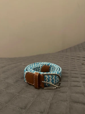 Ljusblå vit flätat bälte - Tja det är helt nytt från Bältgallerian. Det är 105cm långt och 3,5vm brett. Det är i ett elastiskt material så passar större storlekar. Vid köpa av flera minskad priset.