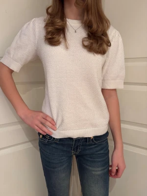 Vit stickad topp med kort ärm - Säljer en vit stickad topp med korta ärmar och rund hals från Vila. Toppen har en grovstickad struktur och ribbade muddar vid ärmslut och nederkant. Perfekt att matcha med jeans eller kjol för en fräsch look. 😍 Storlek M men passar xs-m. Personen på bilden har storlek xs.