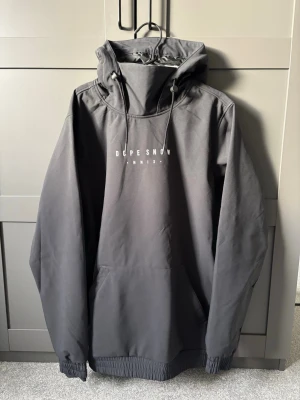 Svart vindjacka från Dope Snow, M - Säljer en svart vindjacka från Dope Snow i storlek M. Jackan har huva med snörning, stor magficka och sidodragkedja för liftkort och liknade. På bröstet står det 'DOPE SNOW MMIX' och på ryggen finns ett färgglatt tryck med berg och sol. Perfekt för dig som gillar streetwear och snygga detaljer nu till skidsäsongen!|Nypris:1800|Storlek:M