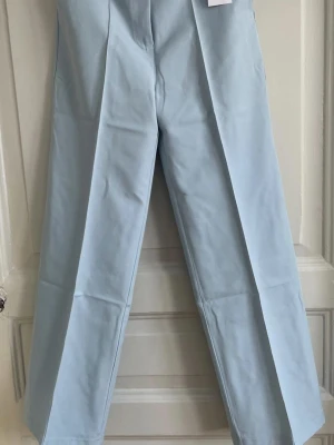 Classic wide pants baby blue Design by Si - Oanvända högmidjade klassiska vida byxor. Dessa byxor är skräddarsydda och har sidfickor och en klassisk sömdesign framtill. Benen är vida och byxorna stängs med knapp och dragkedja. 36-38 (S-M)