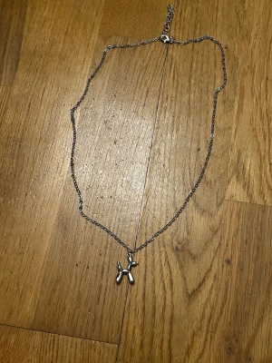 silverfärgad ballonghund-halsband - Unikt halsband med en ballonghund som hänge i silverfärg. Kedjan är tunn men tålig och justerbar med karbinlås. Perfekt accessoar för dig som gillar lekfulla detaljer och vill sticka ut lite extra. Vem kan fråga för mer?