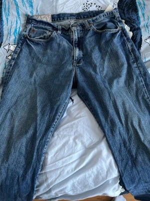 Polo Ralph Lauren blå jeans straight fit - Polo Ralph Lauren jeans i blå denim med rak passform och normal midja. Jeansen har fem fickor, knappgylf och tydliga slitningar för en cool vintage-look. Perfekta för dig som gillar tidlös stil och vill ha ett par riktigt schyssta jeans. Pris kan diskuteras, hojta om du har funderingar!