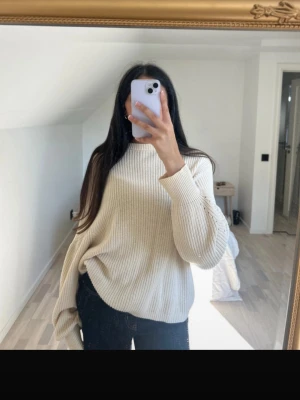Beige stickad oversized tröja - Säljer en beige stickad tröja med oversized passform och långa ärmar. Tröjan har en ribbad struktur och hög hals, perfekt för lager-på-lager under kyliga dagar. Enkel och stilren design som är lätt att matcha med olika outfits.