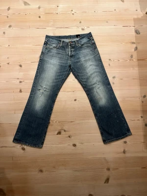Blå baggy jeans från Jack & Jones - Snygga blå vintage jeans från Jack & Jones med bootcut passform. Jeansen har slitna detaljer och ljusare partier på låren och knäna.                              Midja: 44,5cm                                                         Total längd: 98,5cm                                                Ben öppning 24cm
