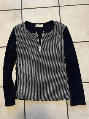 Svart och vit randig långärmad topp - Snygg långärmad topp från Star Lee med svart bas och vita vertikala ränder på framsidan. Rund halsringning och en dekorativ dragkedja framtill. Ärmar och baksida är helsvarta. Perfekt för dig som gillar stilrena detaljer och kontraster.