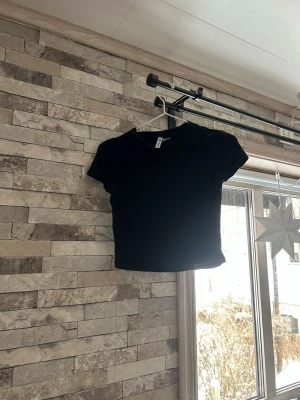 Svart croppad topp från H&M Divided - En enkel svart croppad topp från H&M Divided Basic. Modellen har rund hals, korta ärmar och är tillverkad i mjuk bomull. Perfekt att matcha med jeans eller kjol för en clean look.