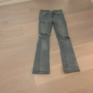 Bootcut ljusblå Lågmidjade jeans med slitningar - Säljer ett par ljusblå Lågmidjade  bootcut jeans i storlek 32 från gina tricot med slitna detaljer och hål på båda knäna. Några missfärgningar på baksidan längst ner vid ena foten men inget som syns tydligt när man har dem på skriv för fler bilder pris kan diskuteras❤️