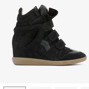 Isabel marant  - Säljer ett par svarta sneakers med inbyggd wedge-klack och coola kardborreband. Skorna har en chunky siluett, rund tå och beige sula. Materialet är mocka och detaljer i skinn, vilket ger en lyxig känsla. Perfekta för dig som vill ha extra höjd men ändå vara bekväm.