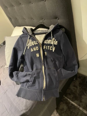 Abercrombie &fitch - Snygg och bekväm hoodie från Abercrombie & fitch. Skön och varm med blå och grå färgkombination. Tröjan har små slitningar men inget överdrivet och den ska ha det. Finns dock en defekt som inte ska va där i längst ut på ena armen se på bilden. Vet ej vad det är har inte försökt ta bort det men antar att de kan försvinna om man försöker. För mer information är det bara skicka meddelande. Priset är ej hugget i sten😊
