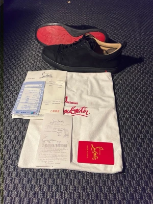 Svarta sneakers från Christian Louboutin - Säljer ett par svarta sneakers från Christian Louboutin i mocka med klassisk röd sula. Skorna har rund tå, snörning och beige innersida. Kommer med dustbag och äkthetskort. Perfekta för dig som vill ha något stilrent men ändå lyxigt.