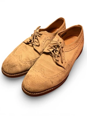 Beige mocka loafers från Gant - Snygga beige loafers från Gant i mocka med klassiska broguedetaljer och snörning. Skorna har rund tå och platt sula, samt dekorativa perforeringar längs kanterna. Perfekta för dig som gillar stilrena och tidlösa skor.