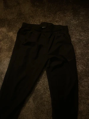 Svarta mjukisbyxor från Nike - Svarta mjukisbyxor från Nike med diskret logga på benet. Byxorna har elastisk midja och två sidofickor. Perfekta för chill eller träning, tillverkade i mjukt material för maximal komfort.