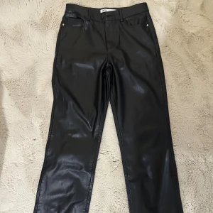 Svarta raka byxor i skinnimitation Zara - Säljer ett par svarta byxor från Zara i skinnimitation med raka ben och klassisk femficksmodell. Byxorna har bälteshällor och stängs med knapp och dragkedja. Perfekta för dig som vill ha en edgy look.