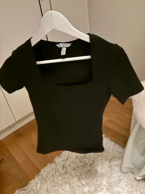 Svart topp med fyrkantig ringning - En svart topp i storlek XS med korta ärmar och snygg fyrkantig ringning. Toppen har en tight passform. Använd nån enstaka gång