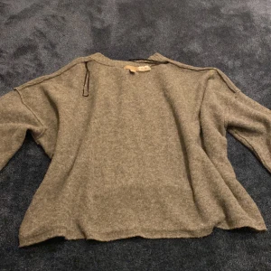 Grå stickad tröja från H&M - Mysig grå stickad tröja från H&M i storlek M. Tröjan har en avslappnad passform med långa ärmar och rund halsringning. Perfekt för kyliga dagar och enkel att matcha med jeans eller kjol.