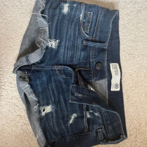 Mörkblå jeansshorts Abercrombie & Fitch - Snygga mörkblå jeansshorts från Abercrombie & Fitch med låg midja och slitna detaljer. Klassisk femficksmodell med fransig kant och coola kontrastsömmar på bakfickorna. Perfekt för dig som gillar en avslappnad och trendig stil.