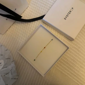 Färgglatt armband från Syster P - Supersött och tunt armband från Syster P i guldton med små pärlor i blått, grönt, rött och gult. Kedjan är fin och diskret, perfekt för att ge lite färg till din outfit. Kommer i original ask med snygg förpackning. Ny pris 499