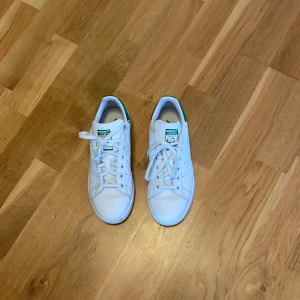 Vita skor från adidas - Ett par vita skor från adidas med gröna detaljer.