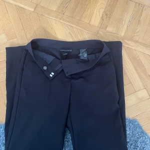 Svarta kostymbyxor från Monki, stl 36 - Snygga svarta kostymbyxor från Monki i storlek 36. Klassisk rak modell med hysk- och hakstängning i midjan. Perfekta för en clean och stilren look. Materialet känns mjukt och följsamt, passar till många olika outfits.
