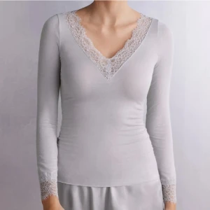 Grå långärmad topp med spets - Supersnygg grå långärmad topp med v-ringning och bred spetskant både vid halsringningen och ärmsluten. Tyvärr har tröjan en fläck på sig(bild 3) men förmodligen försvinner den i tvätten.