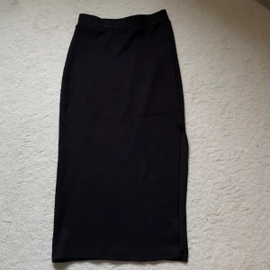 Svart ribbad långkjol - En svart, ribbad långkjol med rak passform. Har en skada där den blivit repad på framsidan därav priset, men det är inget man tänker på 🥰