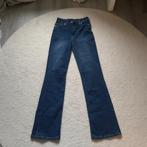 Blå bootcut jeans från Glassx96 - Snygga blå jeans från Glassx96 med klassisk femficksdesign och bootcut-ben. Jeansen har normal midja och är tillverkade i ett mjukt denimtyg som ger en skön passform. Perfekta för dig som gillar en tidlös och avslappnad stil.