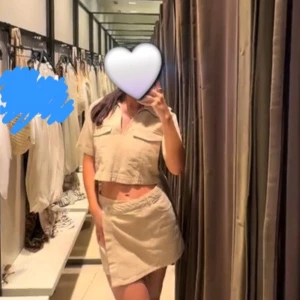 Beige croppad skjorttopp denim från Zara  - Stilren croppad skjorttopp från Zara i beige bomull. Toppen har korta ärmar, två stora bröstfickor med lock och djup v-ringning. Perfekt för en trendig och avslappnad look med utility-vibbar.