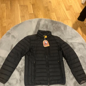 Svart dunjacka från Parajumpers - Svart dunjacka från Parajumpers med klassisk gul detalj vid kragen och broderad logga på ärmen. Jackan har quiltad design, dragkedja framtill och två sidofickor med dragkedja. Perfekt för kyliga dagar och riktigt snygg till streetwear.Jackan är buren 2 gånger andra gången skulle jag öppna innerfickan och en sömn sprättades upl se bild (5)