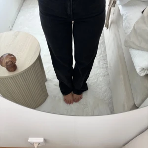 Svarta raka jeans med hög midja - Säljer ett par svarta jeans med hög midja och raka ben. Jeansen har klassisk femficksdesign och dragkedja framtill. Snygg passform som sitter bekvämt över höfterna och faller rakt ner. Perfekta till sneakers eller boots.