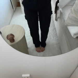 Svarta cargopants med knytband - Säljer ett par svarta cargopants med flera fickor på sidorna och ett snyggt knytband i midjan. Byxorna har en rak passform och är perfekta för en chill och avslappnad stil. Materialet känns slitstarkt och de är riktigt bekväma att ha på sig.