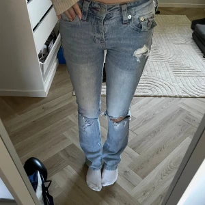 True Religion Becca Bootcut Jeans ljusblå - Säljer ett par True Religion Becca mid rise bootcut jeans i ljusblå tvätt. Jeansen har slitna detaljer vid knä och lår, klassiska bakfickor med broderi och knappar. De finns en liten fläck på ena benet (de är mascara så går förmodligen att få bort) men där av lite lägre pris! 