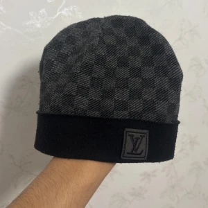 Svart/grå lyxig mössa med rutmönster - Stilren och varm mössa i svart/grå ton med klassiskt rutmönster och diskret logodetalj framtill. Passar perfekt både till vardag och när du vill lyfta din outfit med en elegant accessoar. 	•	Färg: Svart/grå 	•	Material: Mjuk och bekväm stretch 	•	Rutigt mönster med exklusiv känsla 	•	One size – passar de flesta  Mössan är i mycket fint skick och redo att användas direkt. Perfekt för dig som vill ha en premium-look utan att kompromissa.