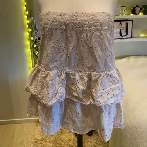 Söt volang klänning - Supersöt beige-vit kort klänning med volanger och broderade blommor. Kjolen har resår i midjan och är gjord i bomull, perfekt för en somrig look. Lätt och luftig med fina spetsdetaljer som ger en romantisk känsla. Är i storlek M men passar båda XS och S💞