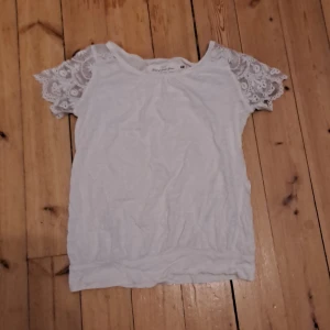 Vit blus med spetsärmar från H&M - Supersöt vit blus från H&M L.O.G.G. med korta ärmar i broderad spets. Toppen har rund halsringning och är tillverkad i mjuk bomull. Perfekt för dig som gillar romantiska detaljer och en feminin look.